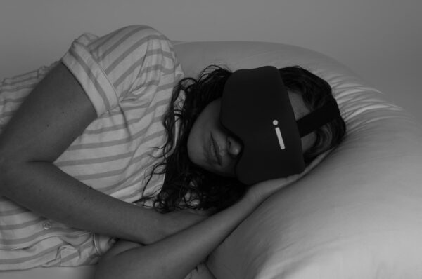En person myser i sängen under dagen, men eftersom hon har en mask så är det kolsvart.